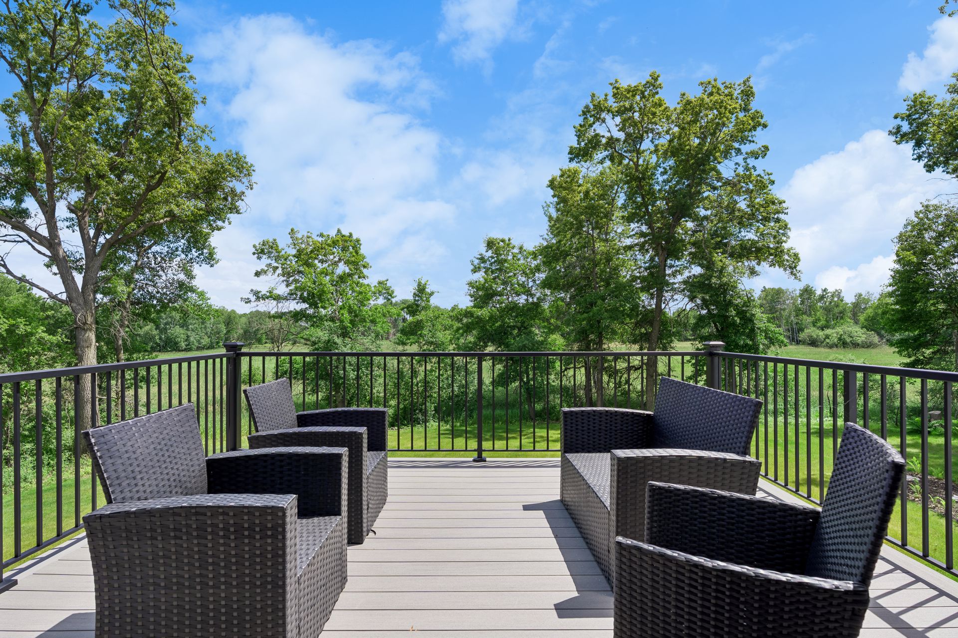 Outdoor deck with seating overlooking wooded backyard and open green space